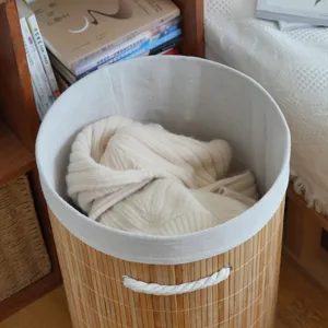 Detail shot of a round bamboo woven storage basket with grey fabric lining and white handles.