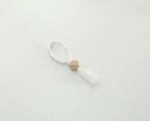 Handcrafted white woven napkin ring with wooden bead and tassel detail for table decor.