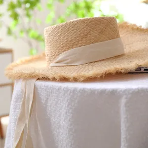 Detail shot of a handmade straw sun hat with a white ribbon and frayed brim on a white table.