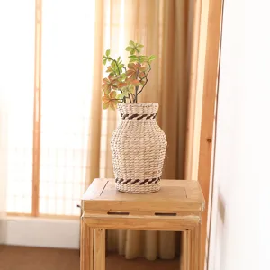 Close-up detail of the hand-woven rattan vase with artificial flower arrangement on wooden stool.