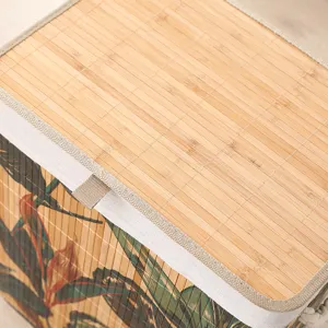 Detalle de cesta de ropa plegable de bambú con tapa tejida natural y estampado tropical.