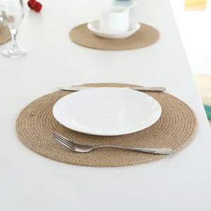 Detailed view of a round woven jute placemat on a clean white table with tableware, perfect for dining.