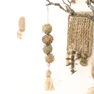 Close up of natural woven grass chew ball pet toy with hanging design and tassel detail.