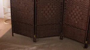 Vista dettagliata di un paravento intrecciato marrone scuro con corda di carta e cerniere metalliche.