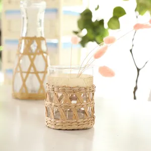 Handmade straw woven glass vase and cup sleeve for creative home decoration and floral display.