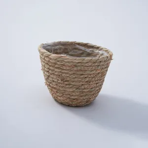 Primo piano dettaglio di piccolo vaso per piante in paglia intrecciata con fodera in plastica.