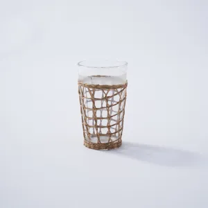 Closeup view of handcrafted woven rattan sleeve on clear glass cup, showing detailed texture.