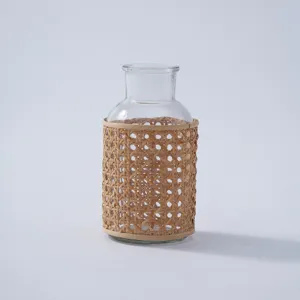 Detailed close up of transparent glass vase with woven rattan sleeve for rustic desktop decoration.
