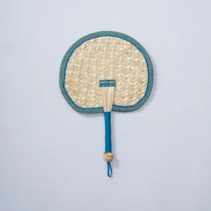 Hand-woven straw fan detail showing blue fabric edge binding and tightly wrapped handle for summer.