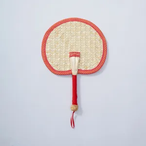 Handcrafted woven straw fan detail with red fabric border and handle wrap for cooling.