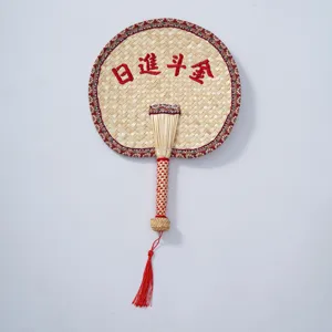 Detailed view of the handmade woven straw fan showing the classic red border and tassel decor.