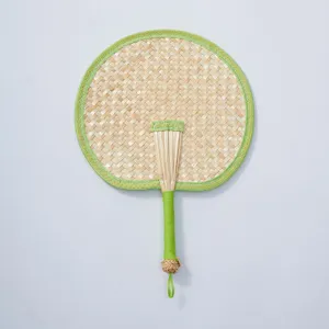 Handmade woven straw fan detail, natural material circular fan with green fabric border.