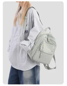 Detail shot of a light green nylon mini backpack worn by a model in a casual striped shirt.