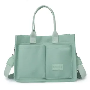 Light green canvas tote bag with double front pockets, top handles and shoulder strap.