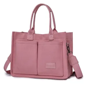 Pink canvas tote bag detail view, featuring dual top handles and external front patch pockets.