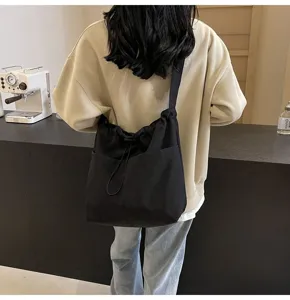 Black nylon crossbody bucket bag detail view featuring drawstring closure and front pocket.