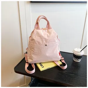 Pink backpack detail view, casual nylon daypack on dark wooden table with book prop.