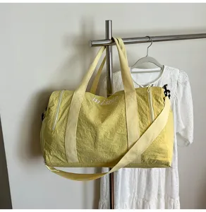 Vue détaillée du sac de voyage jaune montrant la fermeture éclair, la broderie et la sangle.