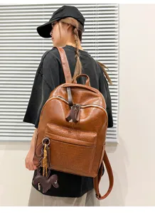 Detail view of brown PU leather backpack featuring crocodile texture front pocket and cute dog charm.