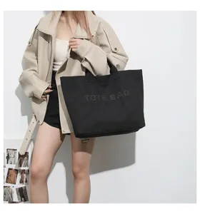 Close-up detail of the black canvas tote bag with studded letter design, casual style.