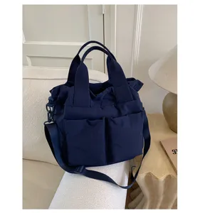 Detail view of the navy blue nylon shoulder tote bag with front pockets in cozy room setting.