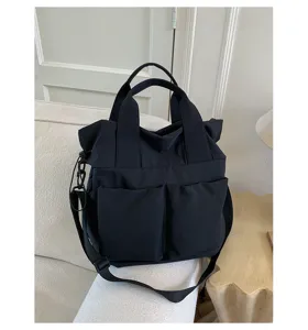 Detail view of a casual black nylon tote bag with dual front pockets and shoulder strap.