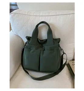 Close-up of dark green nylon tote bag featuring front utility pockets and sturdy handles.