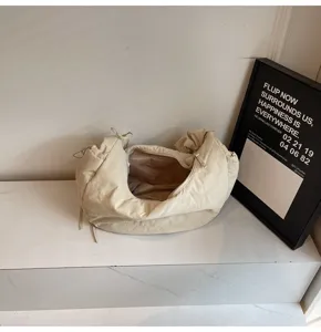 Close-up of beige nylon dumpling bag showing soft cloud design and zipper detail in setting.