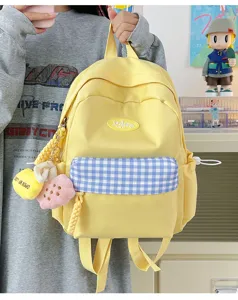 Cute yellow canvas backpack detail with blue plaid front pocket and cute plush pendants.