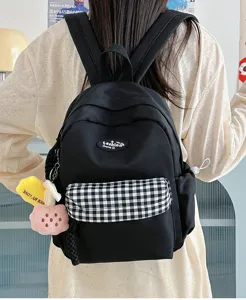 Detail view of black mini backpack with plaid pocket and cute plush charms worn on back.