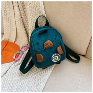 Detailed close-up shot of dark green corduroy mini backpack with cute brown patches.