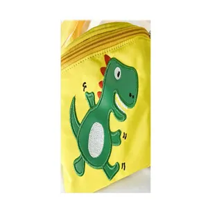 Close-up detail shot of children's yellow crossbody bag featuring cute green dinosaur embroidery.