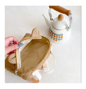 Gedetailleerd overzicht van schattige beige gewatteerde kinderrugzak met oren en ritssluiting.
