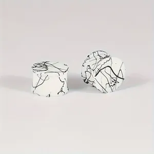Close-up detail of white silicone ear gauges with black splatter design, smooth surface.