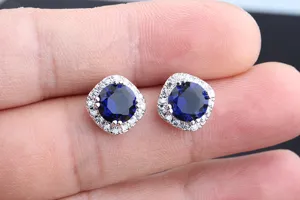 Nahaufnahme von eleganten quadratischen Halo blauen Zirkonia Ohrringen auf den Fingern.