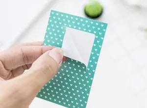 Detailed close-up showing the peeling texture and teal heart pattern of the polaroid sticker.