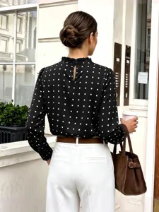 Detailansicht einer schwarz-weißen langärmeligen Bluse mit Pünktchen und Rüschenkragen.