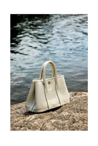 Detail view of a luxury cream leather garden handbag resting on natural rock by water.