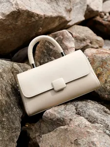 Minimalist beige leather top handle handbag showcased on natural stone background.