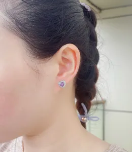 Nahaufnahme Detail von violetten Herz Zirkon Ohrringen am Ohr, glitzernder Kristallschmuck.