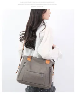 Detail view of a large capacity canvas shoulder bag in gray with brown straps and zippers.