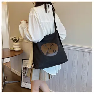 Gros plan d'un sac bandoulière en toile noire avec patch rond marron, style décontracté quotidien.