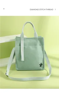Detail view of light green canvas shoulder bag with white strap and front leaf pattern.