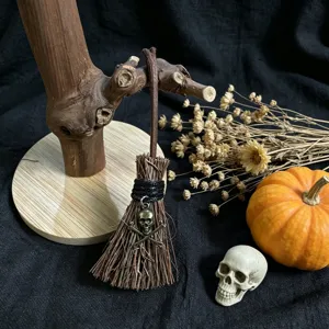 Close-up of a miniature decorative Halloween broom with a skull pendant on dark background.