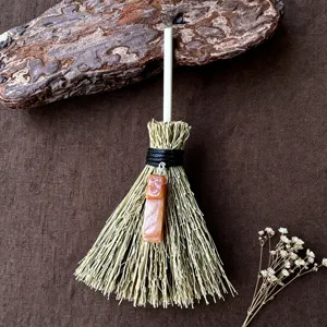 Dettaglio della mini scopa della strega con paglia naturale e ciondolo in cristallo arancione.