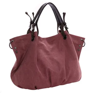 Close-up detail of wine red canvas handbag with dark handles and metal hardware accents.