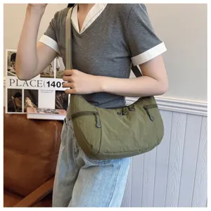 Detail shot of a casual olive green nylon crossbody bag worn by a model, showing the zipper.