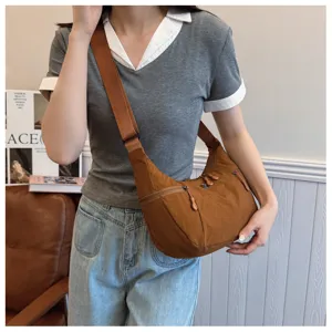 Detailed view of casual brown nylon crossbody hobo bag worn by model, showing zipper pocket.