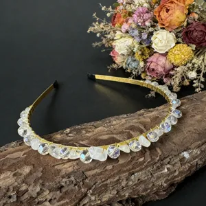 Nahaufnahme des goldenen Kristallhaarreifens auf Baumrinde mit getrocknetem Blumenhintergrund.