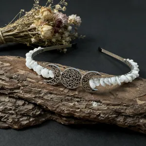 Close-up of handmade crystal gemstone moon headband resting on rustic tree bark with dried floral decor.